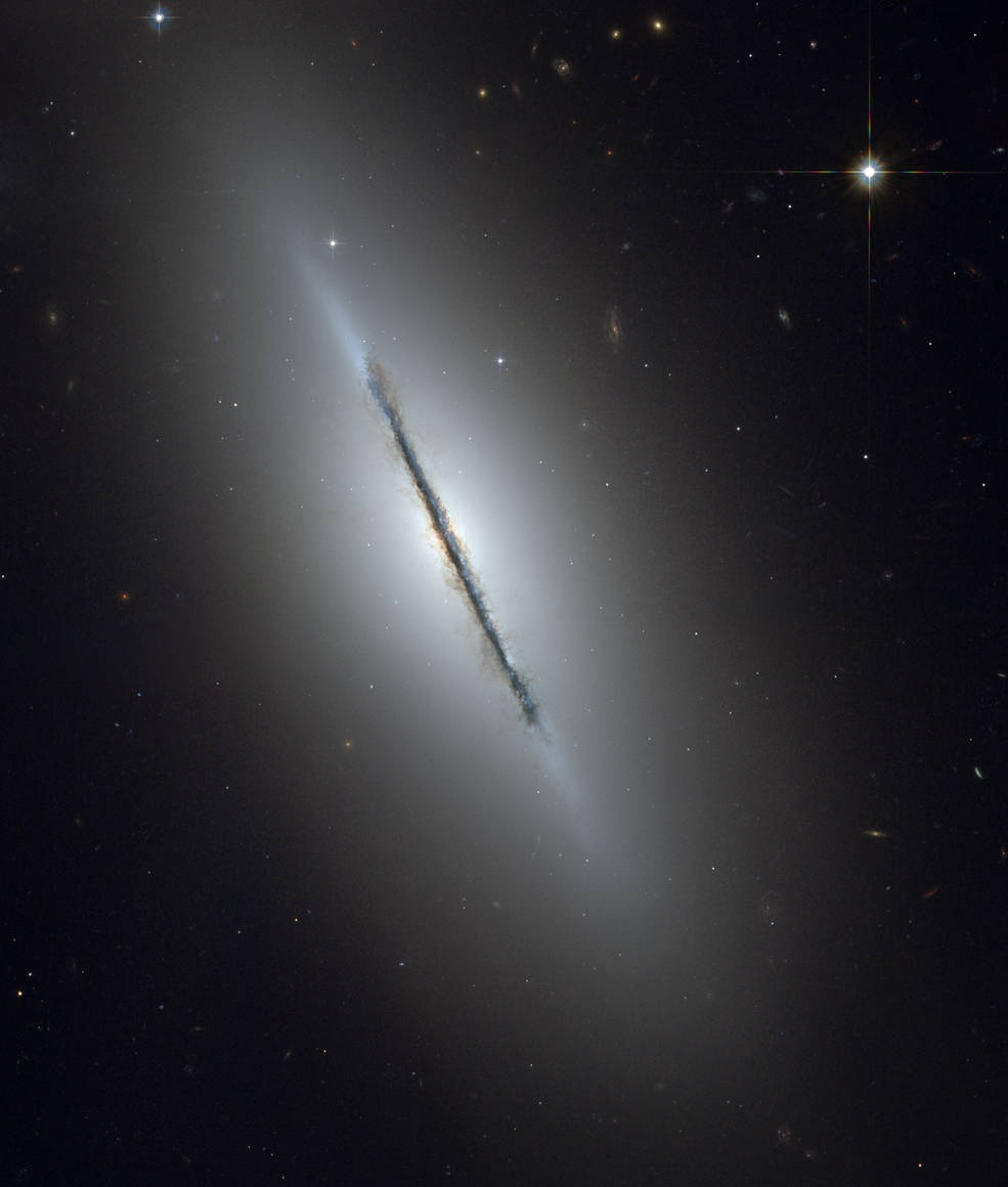 Zdjęcie głębokiego nieba. Odwrócona krawędzią do obserwatora galaktyka na tle nielicznych dalszych obiektów.