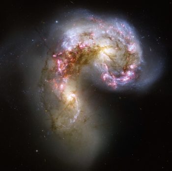 Dwie galaktyki, jedna bardziej żółta, a druga bardziej niebieska, znajdujące się bardzo blisko siebie i połączone ciemniejszym pasem.