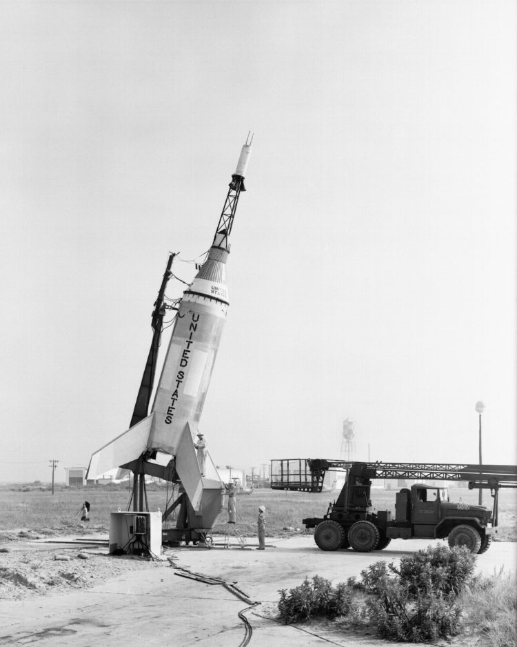 Czarno-białe zdjęcie - rakieta Little Joe na platformie startowej. Obok niej jest samochód