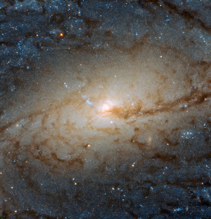 Zdjęcie głębokiego nieba. Zbliżenie na jasne centrum galaktyki. Dookoła niego brązowa spirala, przy krawędziach zdjęcia niebieskie gwiazdy.