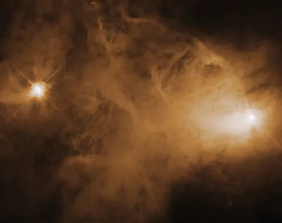 Jasna mgławica emisyjna (obłok gazu i pyłu) rozświetlona na żółto, po lewej i prawej stronie z chmury wyłaniają się dwa jasne punkty, będące gwiazdami