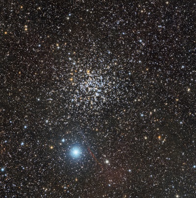 Gromada gwiazd z prawie koncentrycznie ułożonymi wokół jej środka gwiazdami. W tle mniejszy, bardzo jasny obiekt.