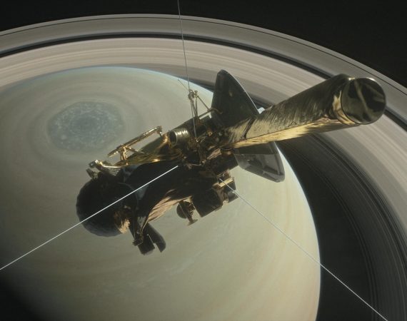 Na środku ilustracji jest sonda kosmiczna, w tle widać północną półkulę Saturna z sześciokątną burzą oraz pierścienie wokół planety.