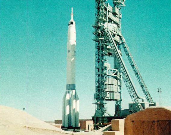 Podłużna biała rakieta obok wysokiej stalowej płaskiej konstrukcji.