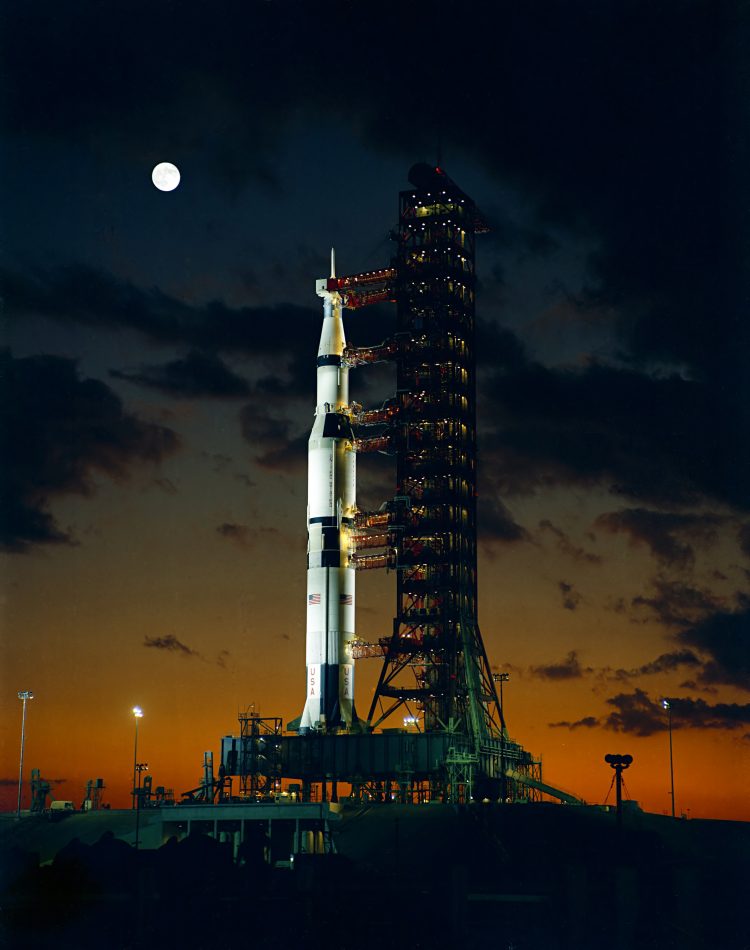 Noc; rakieta Saturn V na wyrzutni, w tle Księżyc