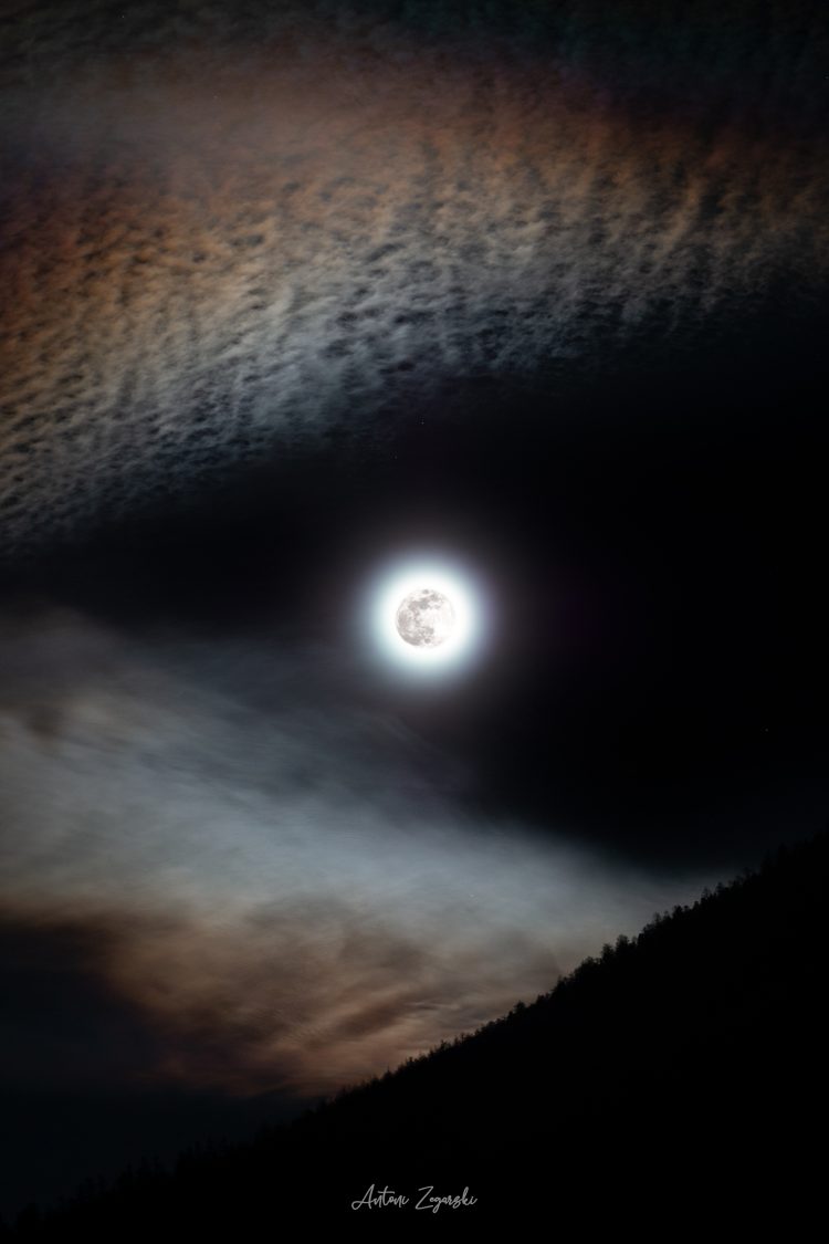 Pełnia Księżyca otoczona z lewej strony chmurami zabarwionymi na pomarańczowo, tworzącymi tzw. „lisią czapę”.