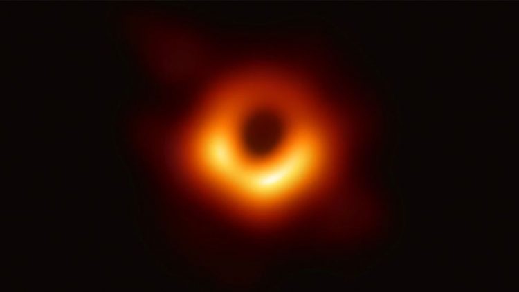 W centrum znajduje się czarna dziura otoczona pomarańczowym dyskiem akrecyjnym. Całość jest na czarnym tle.