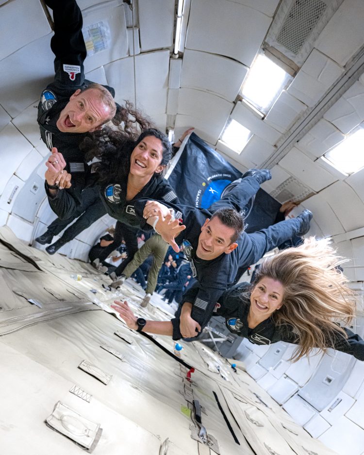 Astronauci misji w czarnych skafandrach wiszą nad ziemią w stanie nieważkości. Znajdują się w białym pomieszczeniu, które jest w rzeczywistości wnętrzem samolotu w czasie spadania, co pozwala osiągnać stan zerowej grawitacji.
