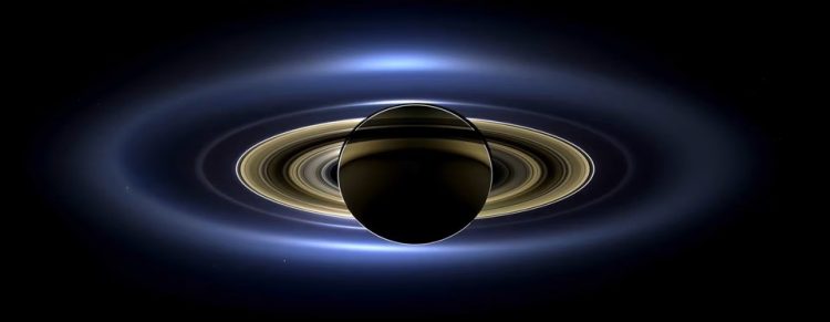 na czarnym tle widnieje ciemna kula okolona jasnymi pierścieniami - Saturn. Najbardziej zewnętrzny pierścień jest lekko rozmyty.