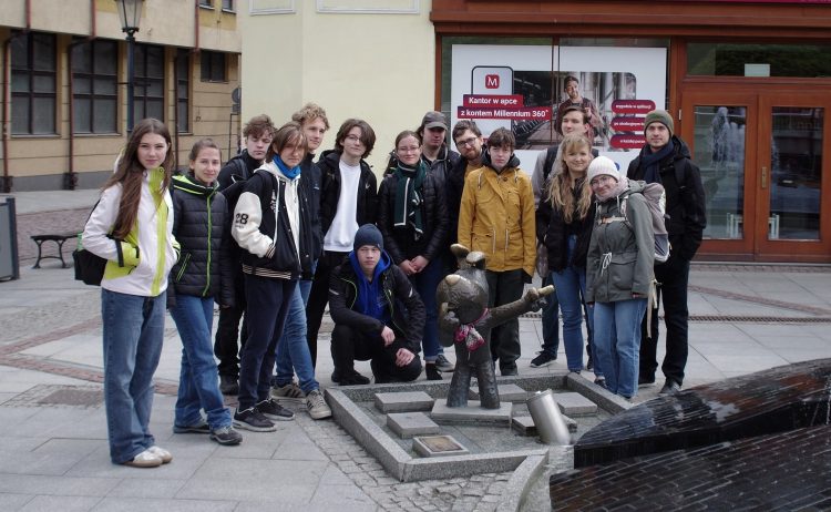 Grupa stoi w centrum miasta za figurą przedstawiającą postać Reksia.