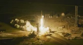Start rakiety Falcon 9 nocą z platformy 39A na Florydzie. Wokół rakiety strumień ognia i dymu.