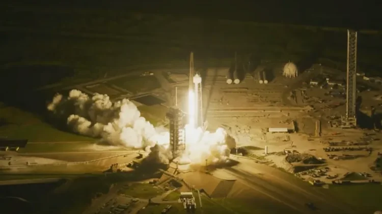 Start rakiety Falcon 9 nocą z platformy 39A na Florydzie. Wokół rakiety strumień ognia i dymu.