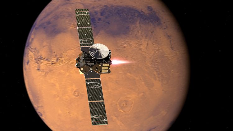 Na czarnym tle widnieje czerwona kula - Mars, na której tle znajduje się czarny satelita z długimi, prostokątnymi panelami słonecznymi. 