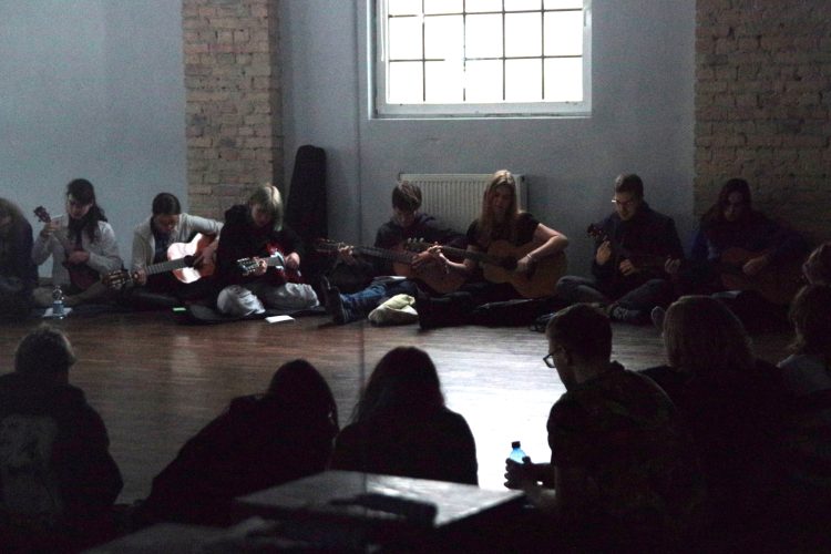 Uczestnicy w kręgu na podłodze podczas śpiewania.