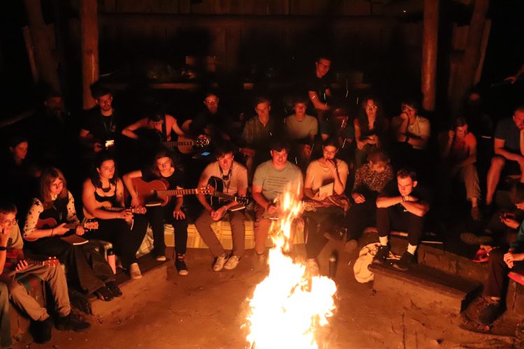 Grupa ludzi otaczająca ognisko po zmroku.