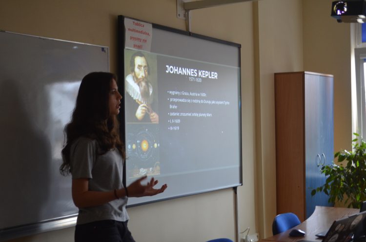 Dziewczyna stojąca przed tablicą, obok niej wyświetlony slajd z prezentacji.