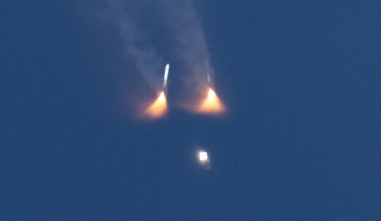 Widok na dwie rakiety pomocnicze SLS zaraz po odłączeniu od głównego modułu w drodze na Ziemię, widać również sam SLS. Od rakiet rozpościerają się w kształcie trójkąta płomienie.