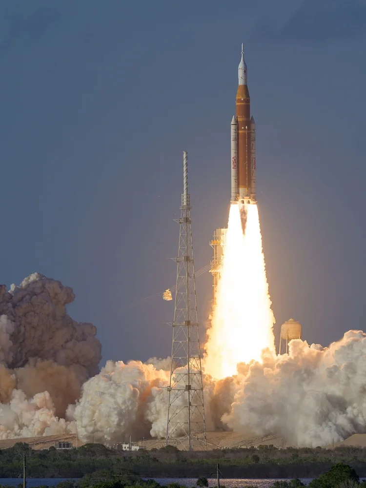 Startująca rakieta SLS na slupie ognia na tle ciemnego nieba.