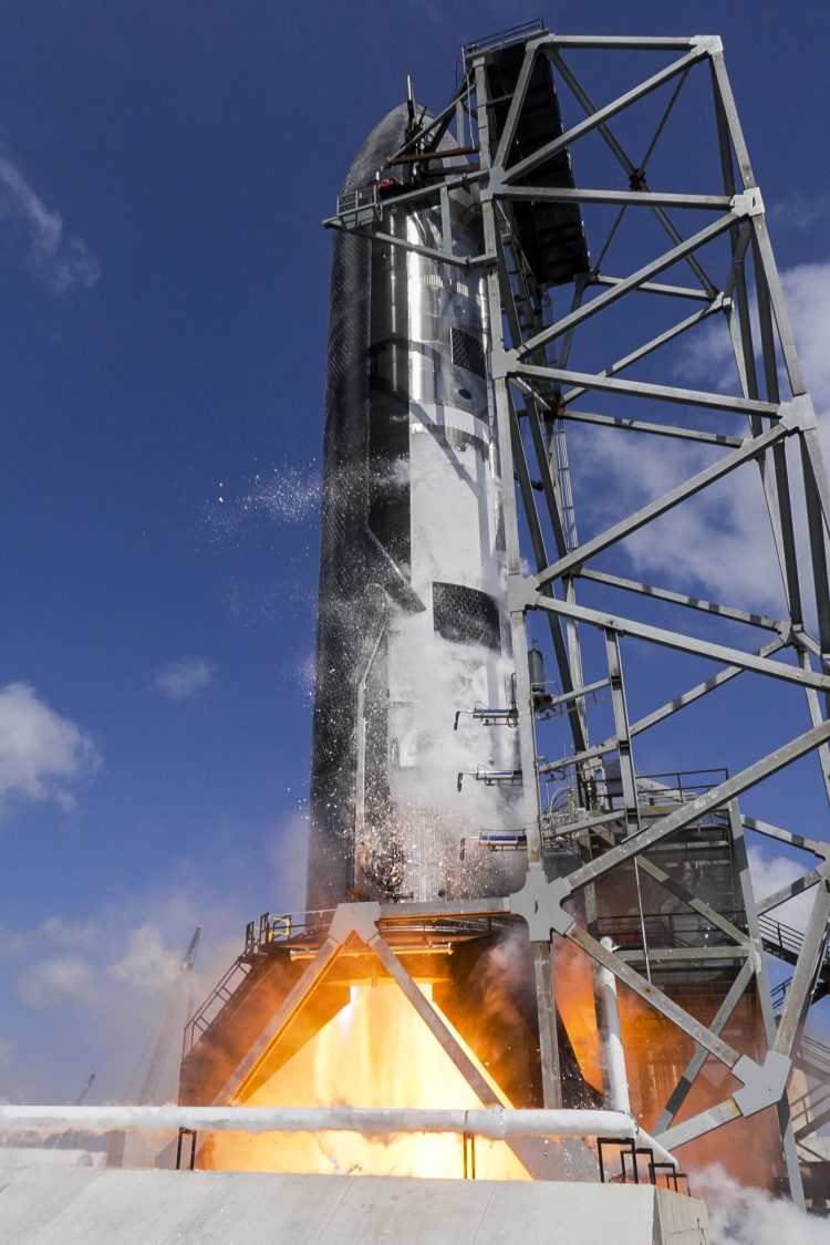  Stojąca na pustym od spodu podniesieniu częściwo pokryta szronem rakieta Spaceship z włączonymi silnikami przy metalowej konstrukcji z prawej.