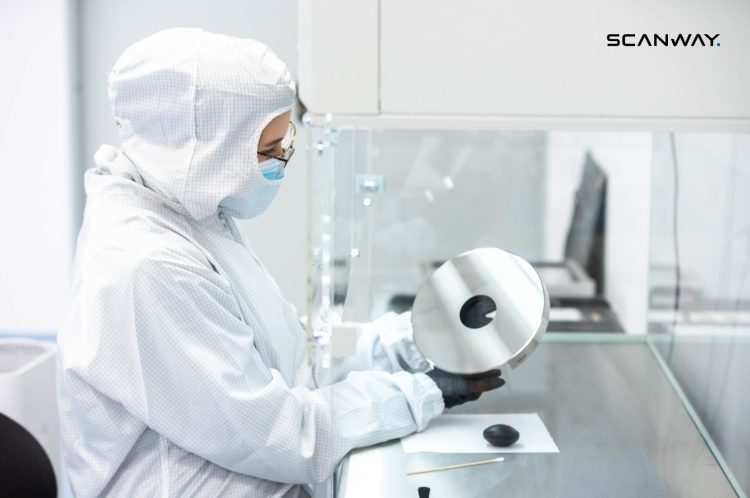 Osoba w białym kombinezonie i rękawiczkach w otoczeniu laboratoryjnym.