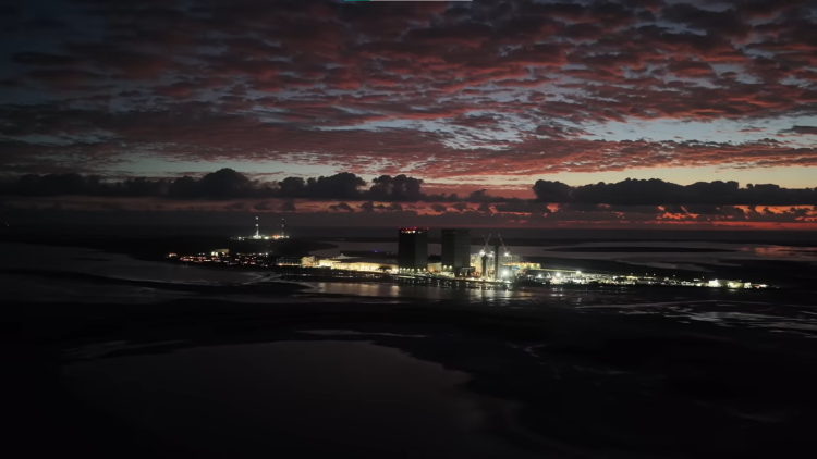 Rozległa instalacja na brzegu morza, widoczna w nocy i rozświetlona przez reflektory.