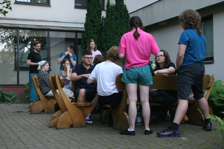 Kadra uczestnicząca w wwk siedząca przy 2 stołach przed białym budynkiem.