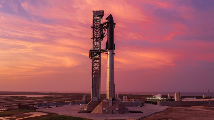 Rakieta Starship stojąca na stanowisku startowym obok wysokiej wieży serwisowej podczas zachodu słońca w ośrodku SpaceX Starbase w Teksasie.