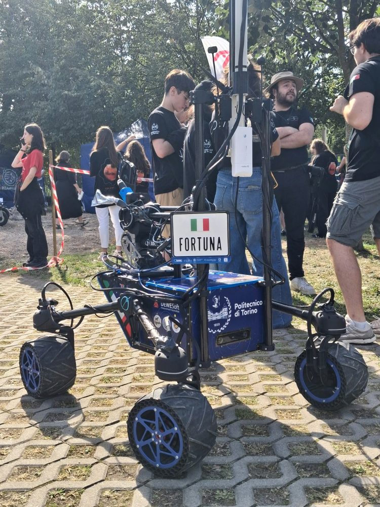 Granatowo-czarny łazik stojący przed grupką rozmawiających osób.