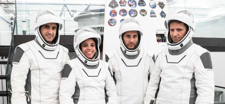 Załoga misji Crew-13 w skafandrach SpaceX podczas przygotowań do lotu na Międzynarodową Stację Kosmiczną. Czworo astronautów pozuje w hełmach przed panelem z naszywkami poprzednich misji.